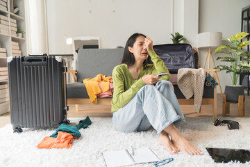 young Asian woman Preparing suitcase for summer vacation trip. Young woman checking accessories and stuff in luggage on the sofa at home before travel.