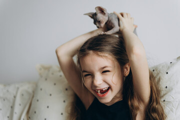 a portrait of a little schoolgirl without 1 baby tooth and her sphinx cat with whom she plays,...
