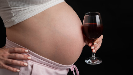 Close-up of the belly of a pregnant woman holding a glass of red wine on a black background. 