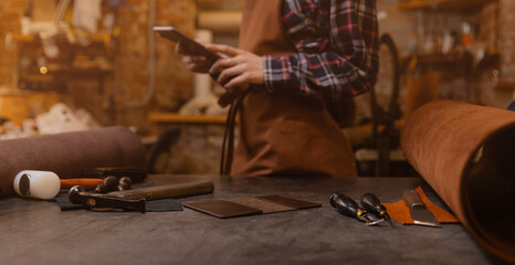 Leather craftsman uses computer tablet for communications on atelier workshop. Concept technology in DIY business banner