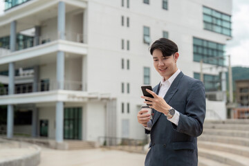 Young Professional Man in Suit Using Smartphone and Holding Coffee Cup Outside Modern Office Building