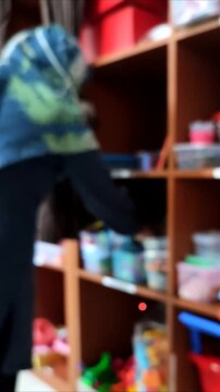 Unfocused abstract background, a therapist wearing a hijab holds a lesson plan and chooses toys to be used.