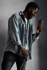 Handsome young African American singer standing with retro microphone singing song on grey...