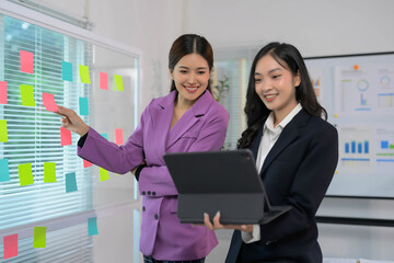 Two Businesswomen Collaborating on a Project with Sticky Notes and a Tablet in a Modern Office