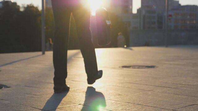 Feet of businessman with briefcase walking in city street at sunset time. Businessman commuting to work. Confident guy being on his way to office. Worker going outdoor. Rear Back view Close up