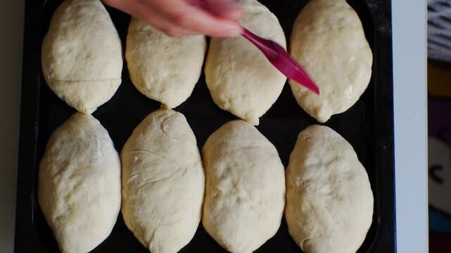 Girl greases portioned pies with vegetable oil for beautiful equally golden crust. Cuisine of peoples of Central Asia. Black baking tray. Overhead view with cinematic look