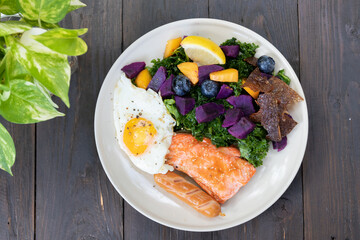 A delicious and healthy meal of grilled salmon, roasted vegetables, and a fried egg.