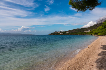 Fototapeta premium Serene coastal scene in tourist town Tucepi along Makarska Riviera, Dalmatia, Croatia, Europe. Pristine pebble beach stretches towards calm, turquoise Adriatic sea in the Mediterranean. Summer travel