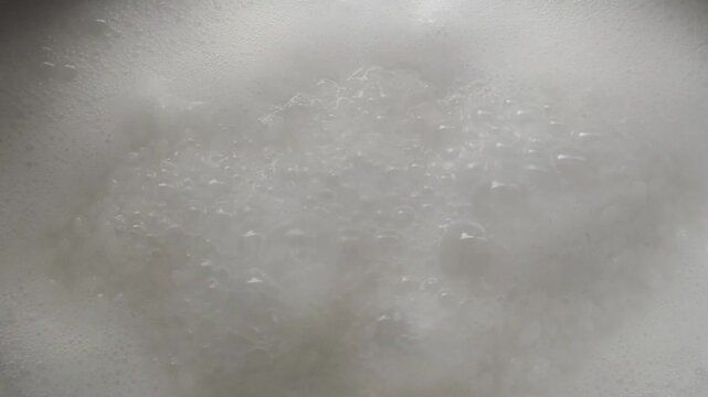 White Kerala matta rice cooked in boiling water with steam and bubbles. Delicious healthy traditional Asian or Indian vegetarian dish preparation concept. 4k closeup macro top view.