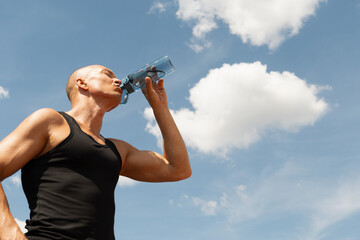 Athletes handsome man drinking water from bottle against blue sky. Concept water balance after active workout. Summer. Close up. Banner.