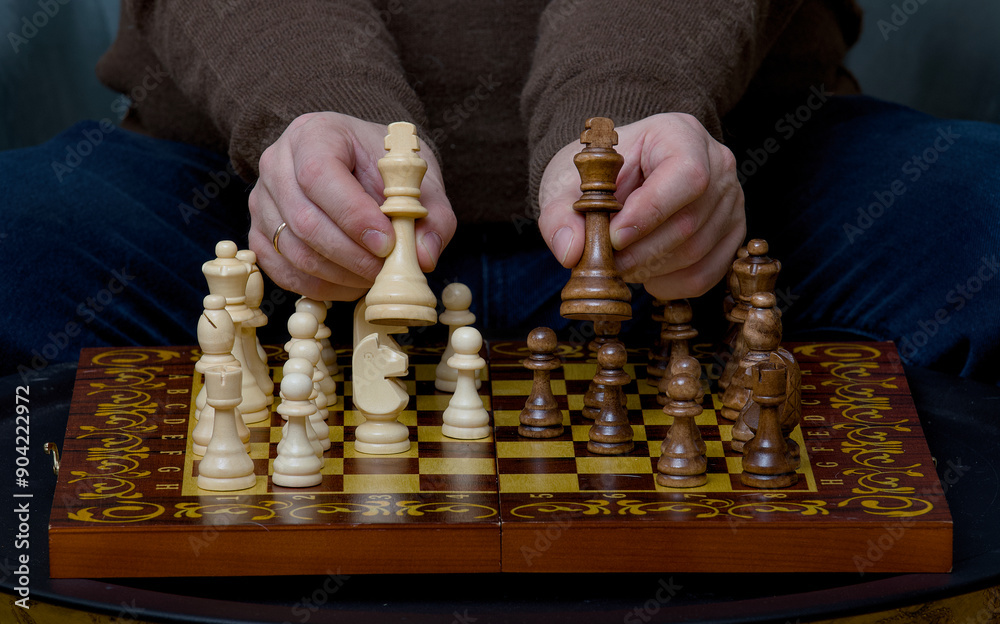 Wall mural hands of a white-skinned man holding two chess pieces over a game board showing them to the camera.