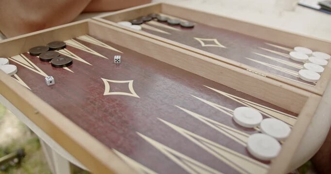 Close-up of hands playing backgammon on a detailed wooden board, highlighting the intricate designs and a white dice.