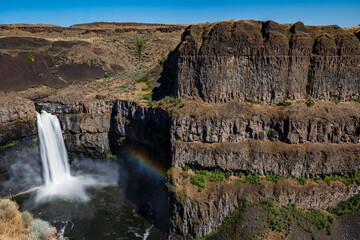 silky waters of Palouse Falls  flowing from the basalt canyon toward the Snake River with a rainbow on the side in Washington State