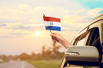 Waving the Paraguay flag against the sunrise or sunset from a car driving along a country road. Holding the Paraguay flag, traveling by car, on a weekend trip.