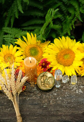 Burning candle, flowers, wheat ears, crystals and symbolic moon amulet in forest, natural...