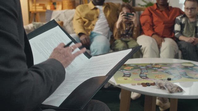 Tilt up view of female social worker with folder of documents sitting opposite to Black young parents and two adopted Caucasian boys asking them questions
