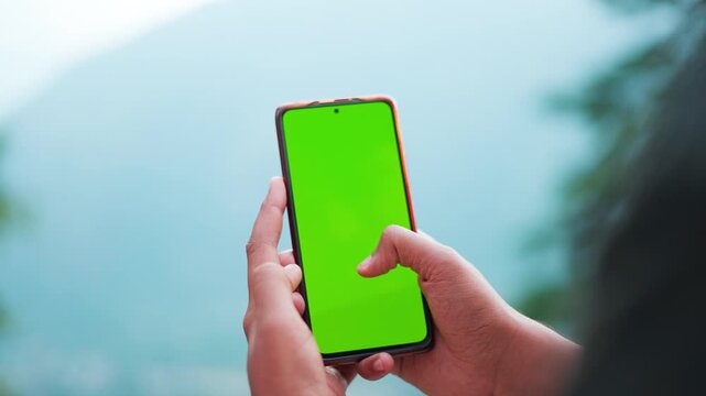 4K Closeup shot of hands of an Indian man holding mobile phone with green screen doing swipe up gesture and scrolling. Chroma key mockup template background. Mobile phone addiction template.