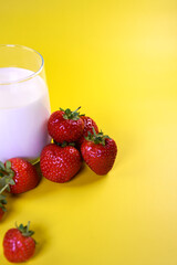 Strawberry milkshake. Glass of milk with fresh strawberries on a yellow background. Berries in a glass.