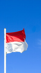 The red and white Indonesia national flag is waving againts clear bright blue sky. free space for text.