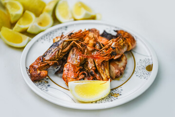 A plate with grilled shrimp and lemon slices on a white background