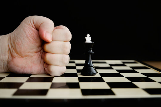 A fist against a black king on a chessboard on a black background close-up, brute force versus mind, overthrowing the ruler, government ultimatum,