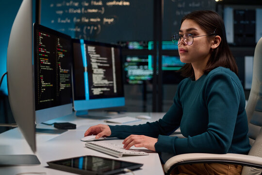 Side view portrait of young woman wearing glasses as cybersecurity engineer typing at computer keyboard and writing code copy space