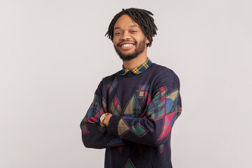 Portrait of handsome joyful cheerful african-american man with dreadlocks and beard standing with crossed arms and looking at camera. Indoor studio shot isolated on gray background.