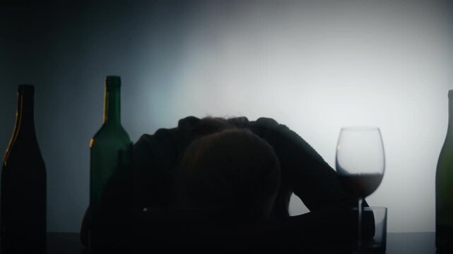 Depressed drunk woman sleeping on desk with empty bottles, alcohol addiction