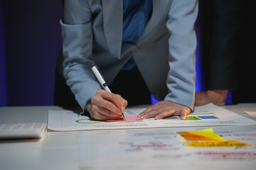 Businesswoman is analyzing financial charts and taking notes on sticky notes while working late at night in the office