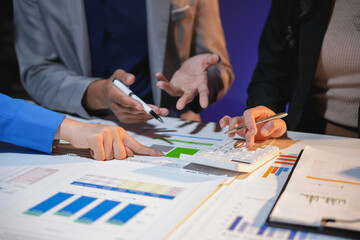 Business team working late, analyzing financial documents and using a calculator to review data and performance