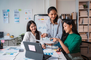 Three asian businesswomen are discussing a project, analyzing charts and working together in a modern office