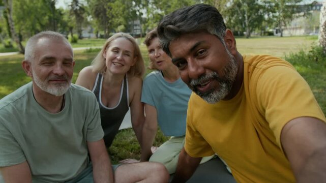 UGC handheld shot of Biracial middle-aged man filming video for vlog with diverse senior friends or having video call, talking after outdoor practice in park on summer day