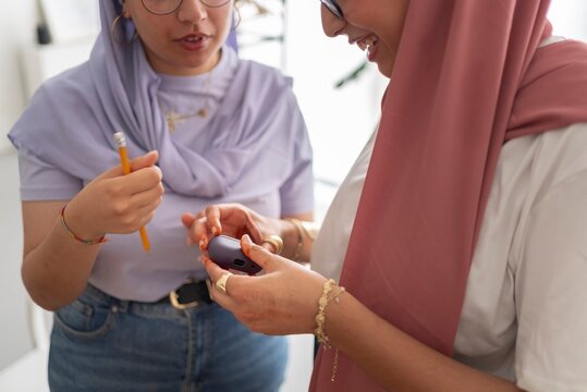 Two women in hijabs review their work together in a modern office, surrounded by various crafting tools and materials, emphasizing collaboration and attention to detail