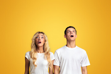 Amazing offer. Shocked guy and girl looking upwards at copy space with open mouth, standing over yellow studio background, panorama