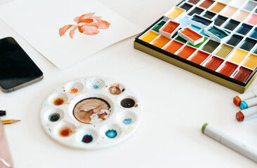 Multicolored watercolor palette, brush, colored pencils and equipment for painting on white desk
