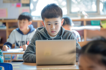 Focused Chinese Schoolboy Working on Laptop in Modern, Brightly Lit Classroom with Classmates