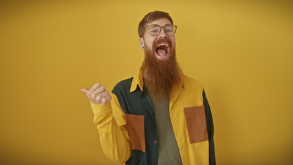 A cheerful young bearded man with red hair wearing glasses gestures thumbs-up against a vibrant yellow background.