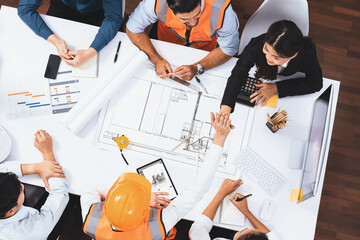 Top view banner of diverse group of civil engineer and client working together on architectural project, reviewing construction plan and building blueprint at meeting table. Prudent