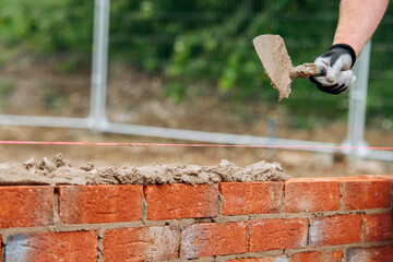 Skilled Mason Carefully Laying Brick With Trowel on Construction Site During Daytime