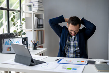 A man is sitting at a desk with a laptop and a stack of papers
