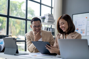 Two people are sitting at a desk with a white board behind them