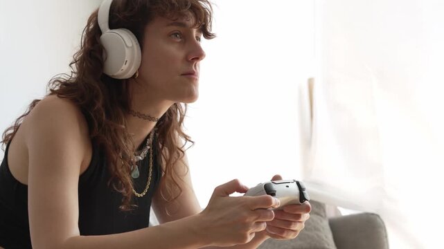 woman playing video games with headphones on her sofa at home