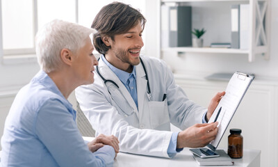 Defeated disease. Happy doctor showing positive test results to senior woman patient at hospital, free space