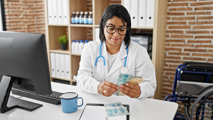 Hispanic woman doctor in clinic examining brazilian real currency indoors