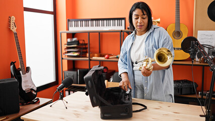 A woman prepares to play a trumpet in a vibrant music studio surrounded by various instruments and recording equipment.