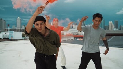 Fototapeta premium Group of multicultural hipster playing color flare at rooftop. Attractive street dancer holding colored smoke and perform break dance move to hip-hop music. Outdoor sport 2024. Hiphop.