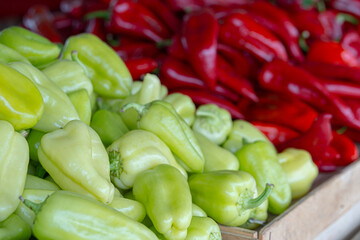 A pile of green peppers and red peppers are displayed in a wooden crate. The contrast between the two colors creates a visually appealing display
