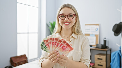 Smiling young woman in office holding israeli shekels, portraying success and finance.