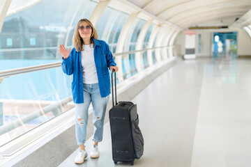 Cheerful Young Woman Waving Goodbye While Traveling With Luggage In Modern Airport Terminal