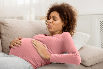 Expectant woman having contractions and doing breathing exercises, lying on sofa at home